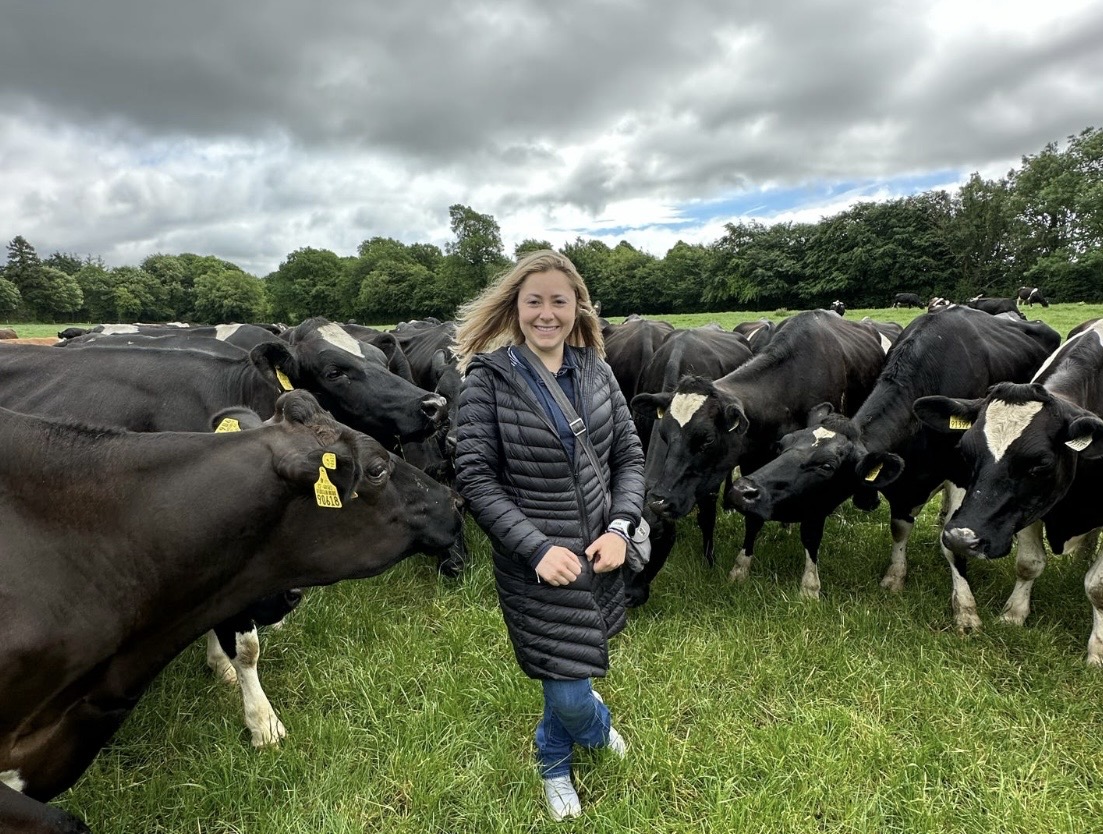 Woman stands in field surrounded by cows
