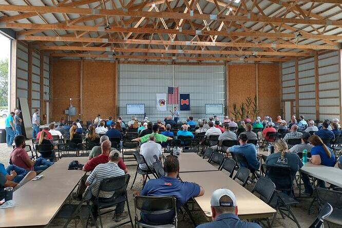 Group of people at tables in a barn with a speaker at the front of the room