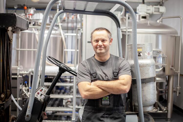 Matt Riggs stands with arms crossed in front of industrial brewing tanks.