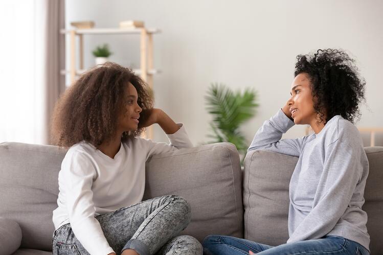 African-American mother and adolescent daughter having a conversation while sitting in a living room sofa