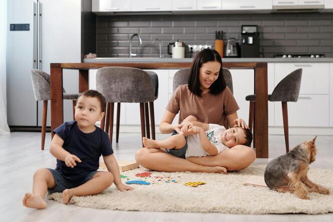 A mother sits on floor to play with her two toddlers