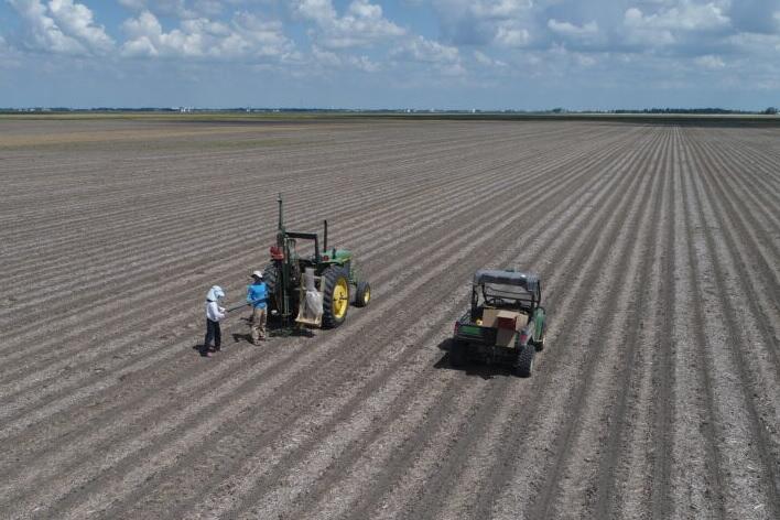 A bare-soil field with two farm vehicles and two people standing nearby