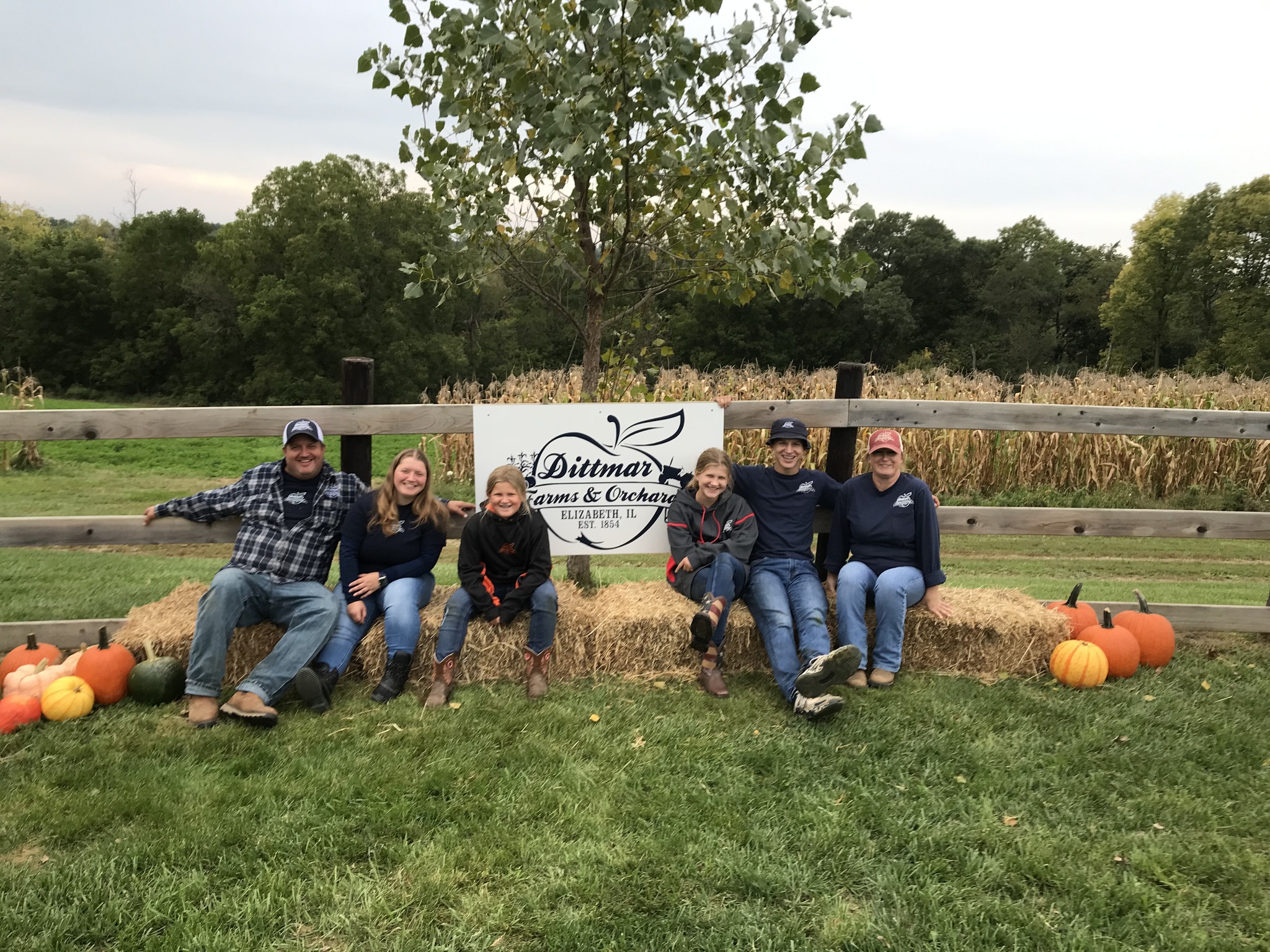 The Dittmar family smiling by the Dittmar Farms and Orchard sign.