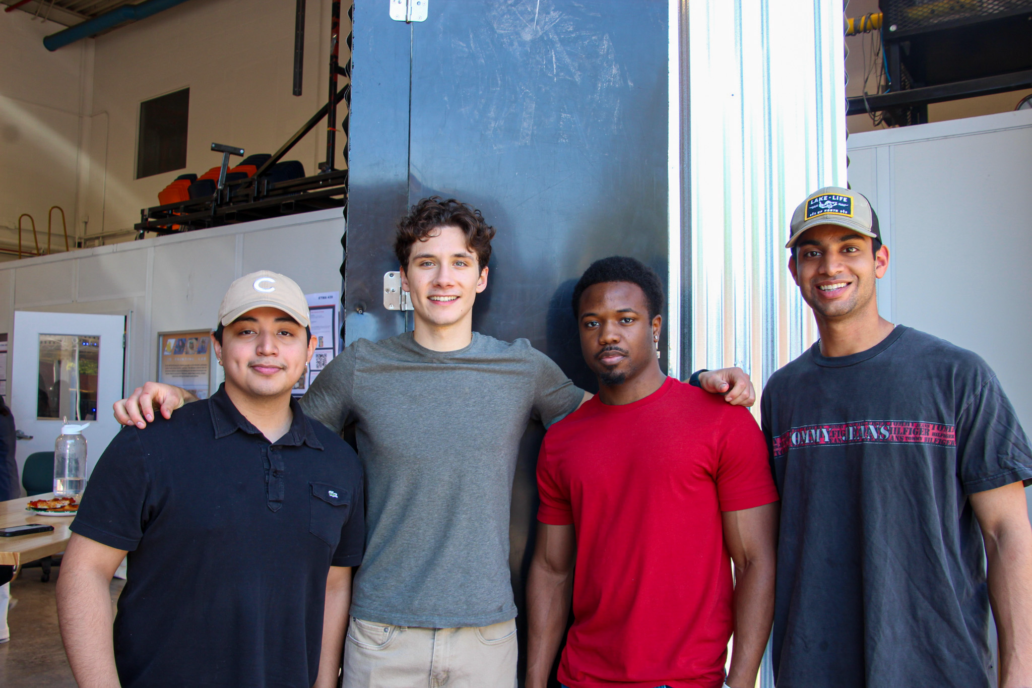 Four young men standing together and smiling in a workshop environment.