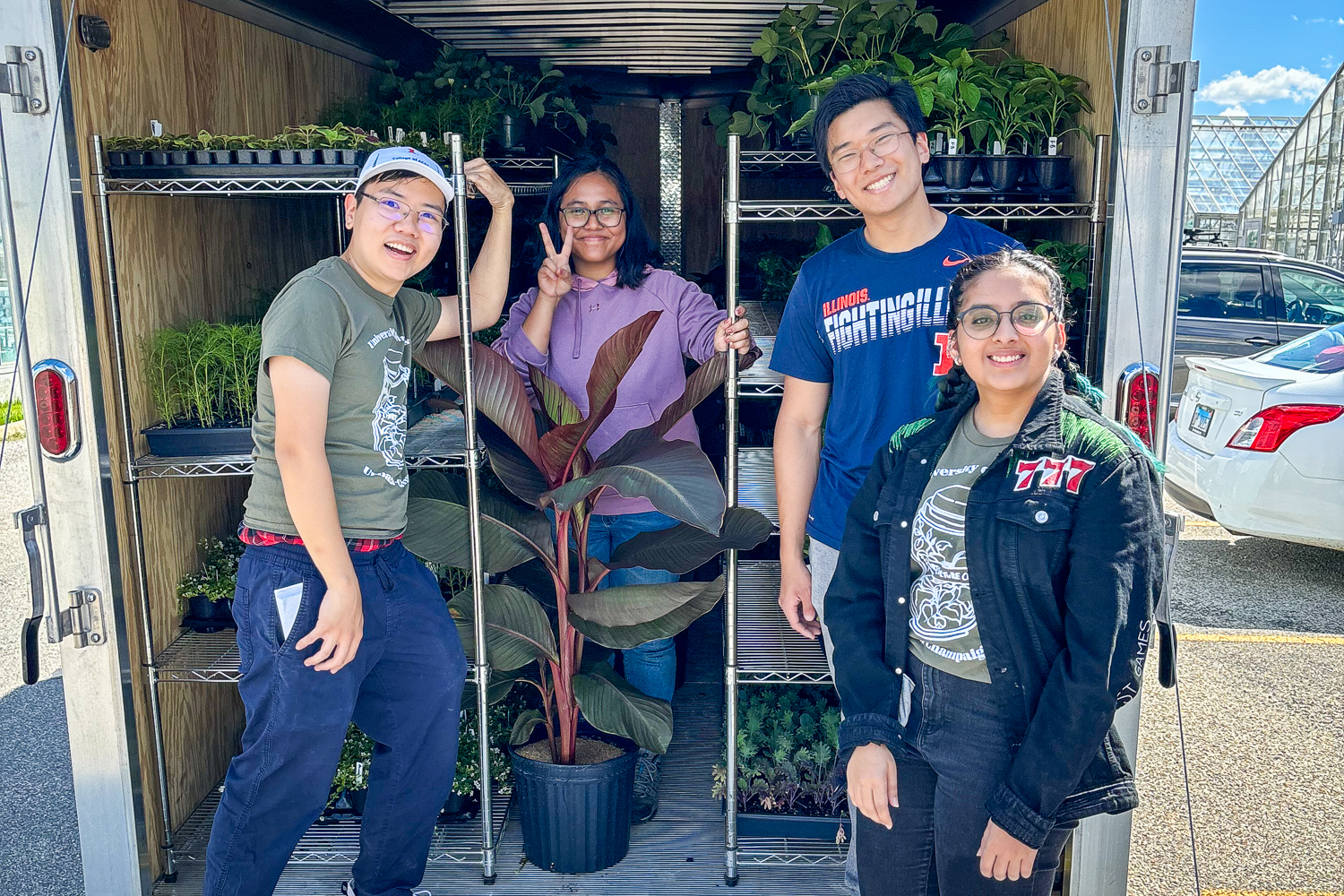 Four students smiling inside a plant-filled trailer on a sunny day.