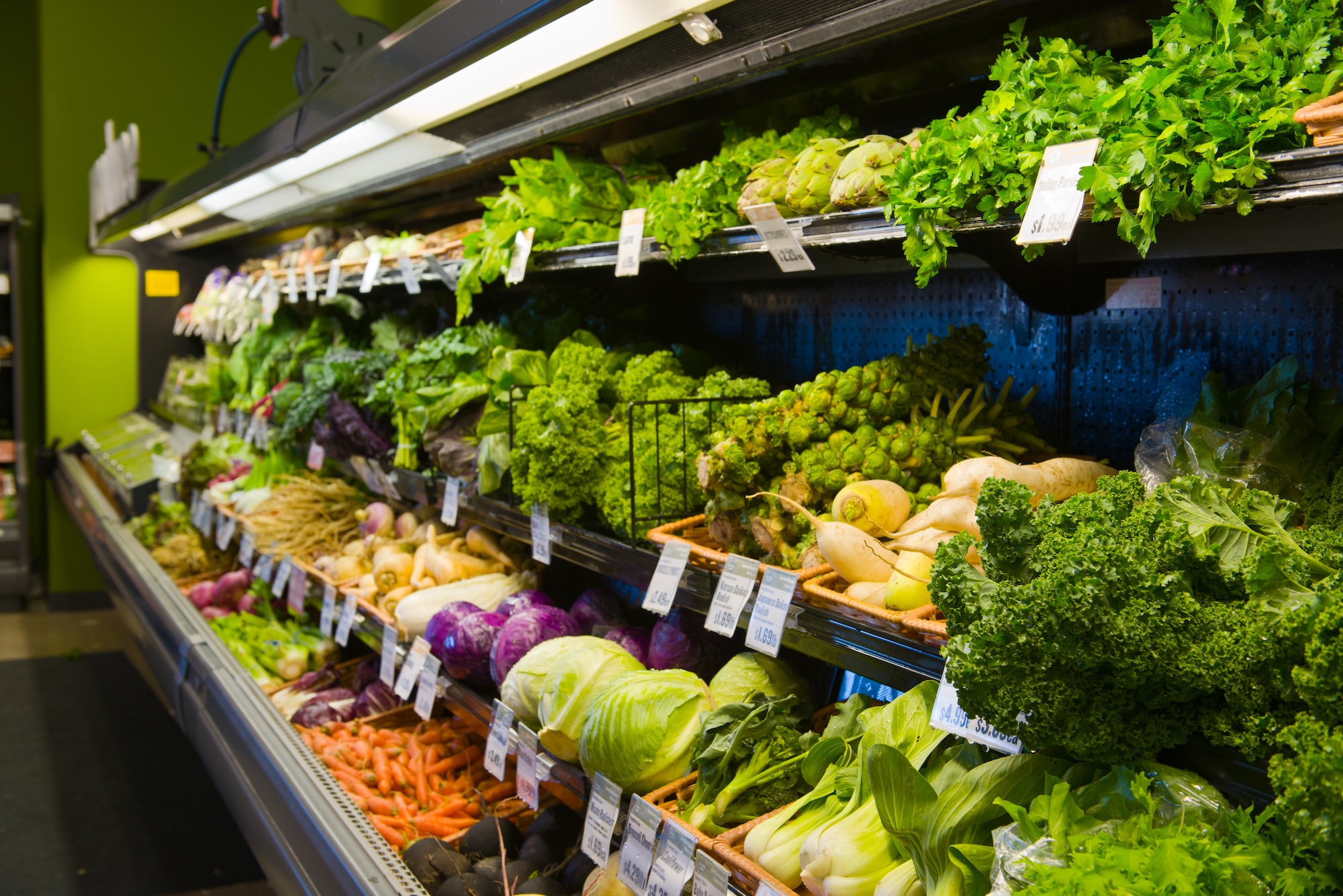 A grocery store produce section displays a variety of fresh vegetables and greens.