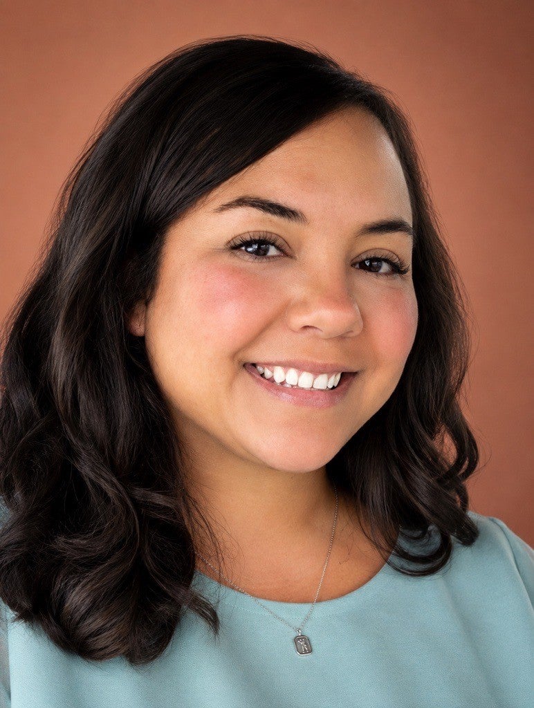 Nikki Camden is a biracial female, with shoulder-length brown hair. In this picture, she is wearing a green shirt and smiling at the camera.