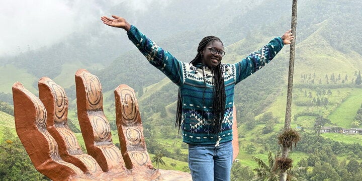 ACES student standing on a large hand in Colombia with her arms up
