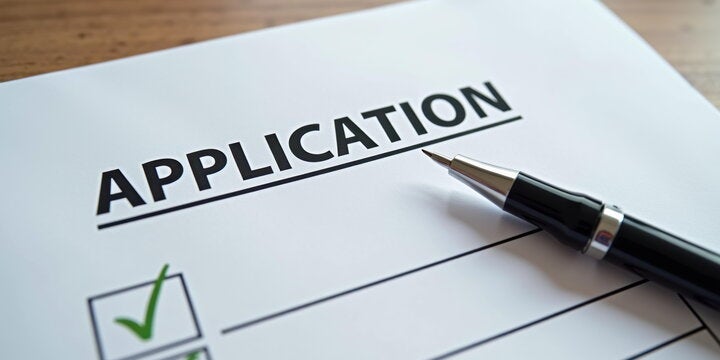 Close-up of an application form with "Application" on it and a black pen resting on the side.