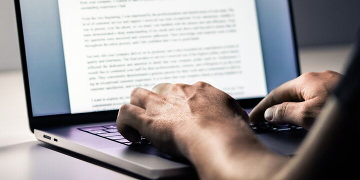 Close-up of hands typing on a laptop with a document open on the screen.