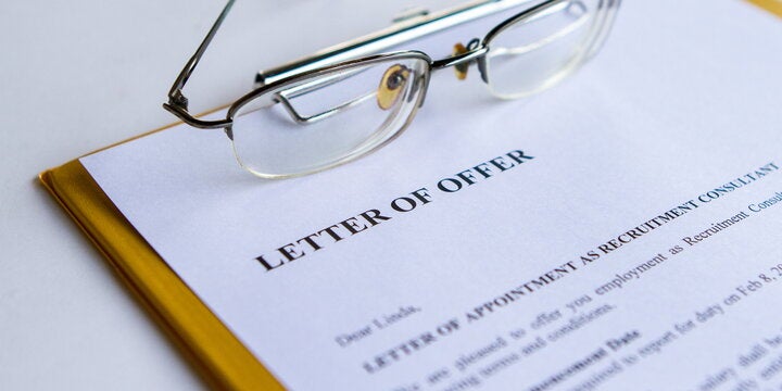 A document titled "Letter of Offer" on a clipboard next to a pair of glasses on a desk.