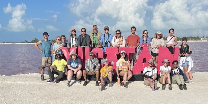A group of students surrounding a Yucatan sign on the beach in Mexico. 