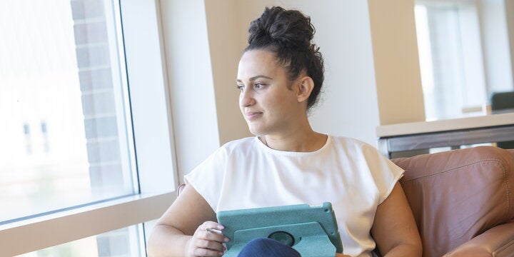 An ACES student in the Funk Library, sitting in a chair and looking out the window.
