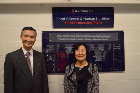 Tai (Terry) Shin stands with his wife You H. (Catherine) Shin in front of a sign for the Food Science & Human Nutrition Pilot Processing Plant.