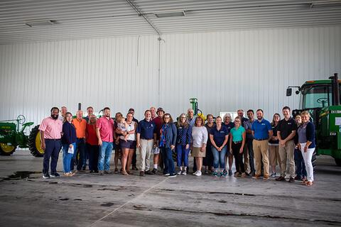 McBride Farm dedication attendees stand in a large group in the machine shed in front of John Deere tractors.