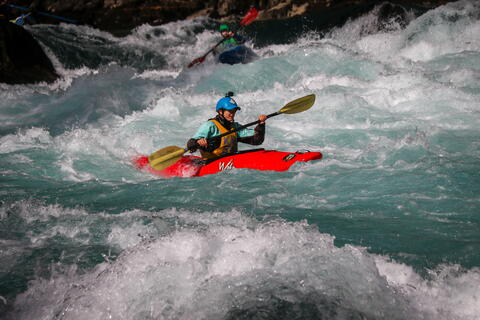 Elizabeth Bruns kayaks whitewater rapids in an orange kayak with a blue helmet.. 