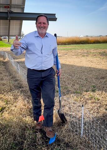 Dean Bollero holds a shovel beside a solar panel.