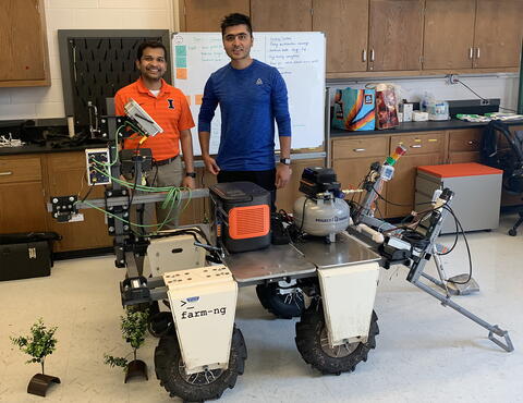 Two men standing by a robotic weeding machine in a lab