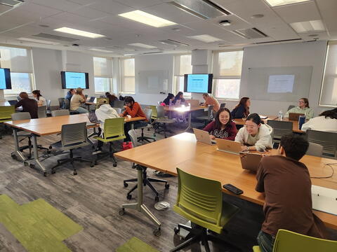 Students in a classroom work together on laptops.