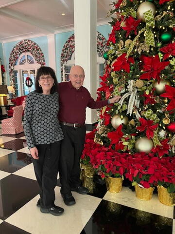Ellen and Jim Holmes stand beside a Christmas tree.