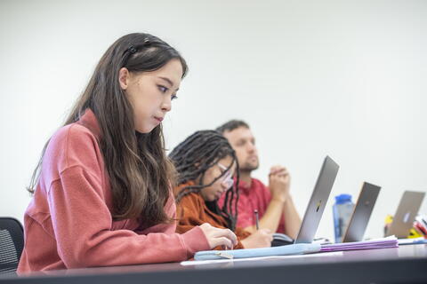 Three students attending a lecture, taking notes on their laptops.