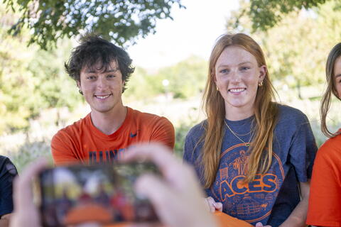Two ACES students sitting in front of a camera, getting their photo taken.