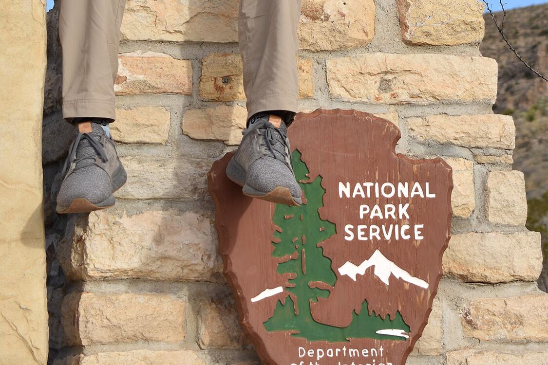 Alex Brockamp's feet dangling in front of a National Park Service sign