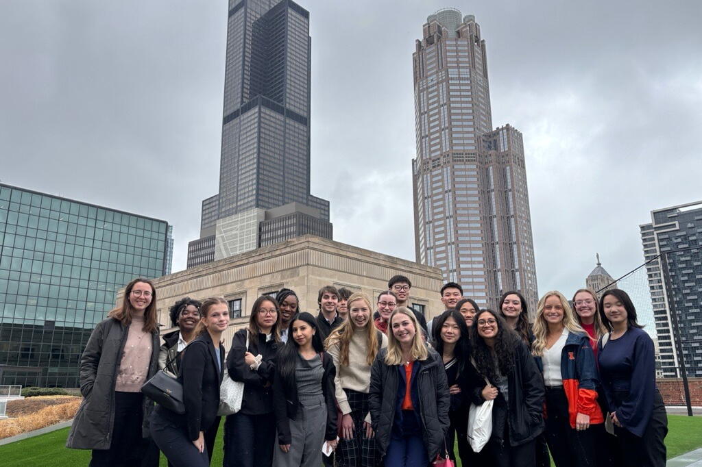 A group of students pose on a rooftop with Chicago skyscrapers visible in the background