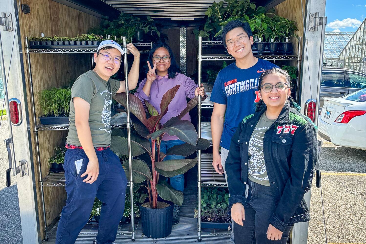 Four students smiling inside a plant-filled trailer on a sunny day.