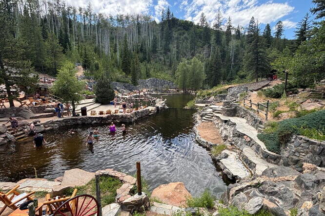 People soak in a spring in front of a forest landscape