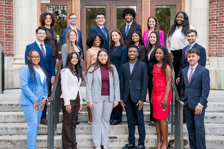 20 homecoming court members in business professional attire stand on steps.