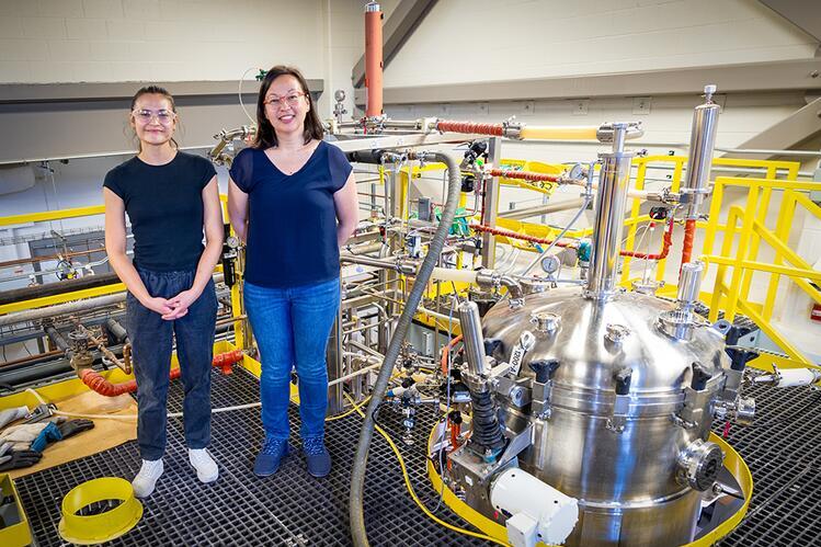 Two individuals stand in an industrial facility.