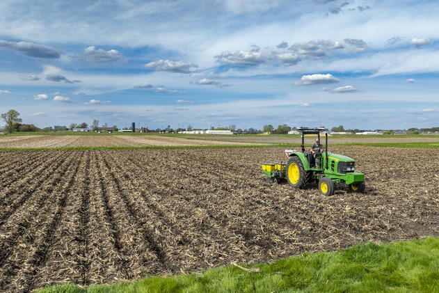 A tractor drives across a harvested field with blue skies in the background