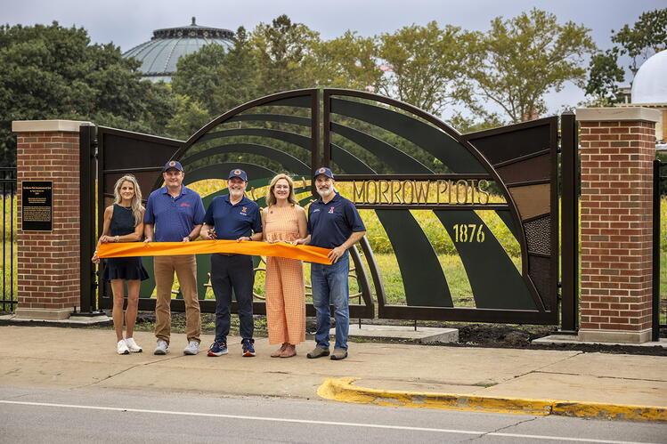 Five people stand behind an orange ribbon in front of the newly constructed Morrow Plots gate