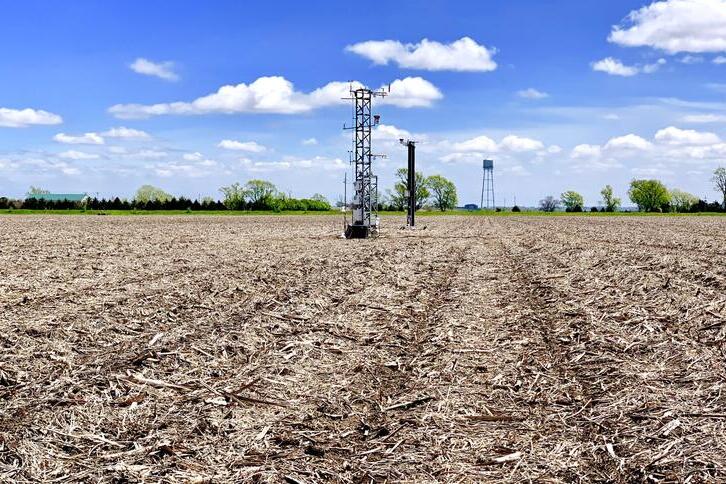 A bare agricultural field showing some crop residue on the surface of the soil. In the distance are instrument towers.