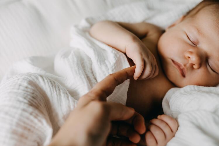 Sleeping infant holding an adult's finger