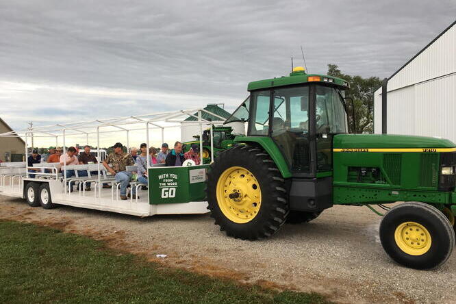 A green tractor pulls a platform with people seated on benches.