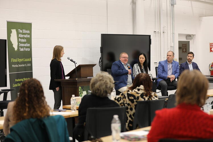 Four panelists and moderator speak in front of a crowd. 