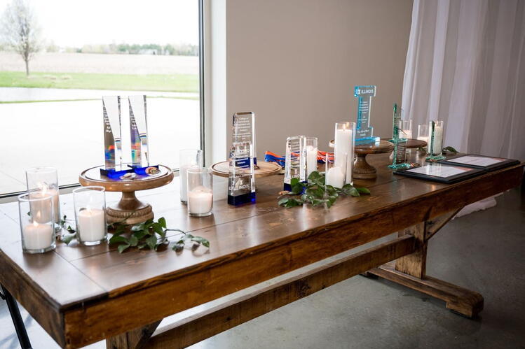 An array of glass award trophies sit on top of a brown wooden table