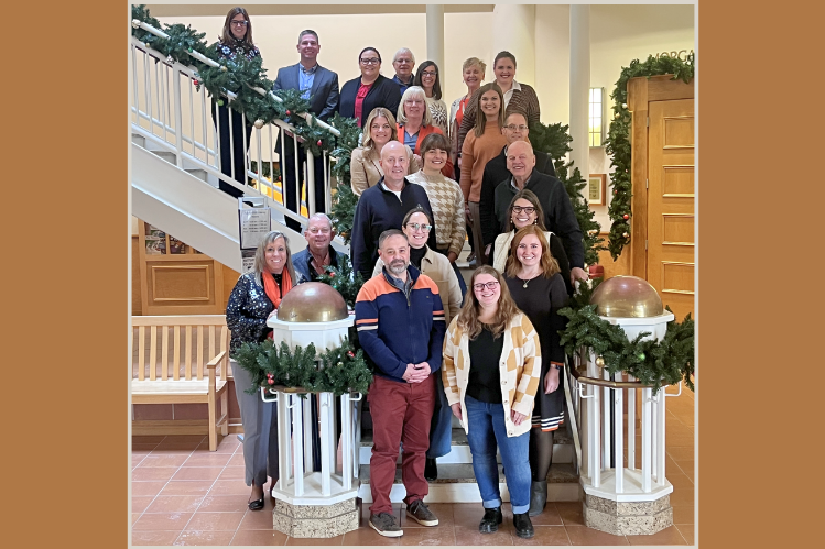 The alumni board and Cora Dittmar stand on a staircase adorned with a festive holiday garland