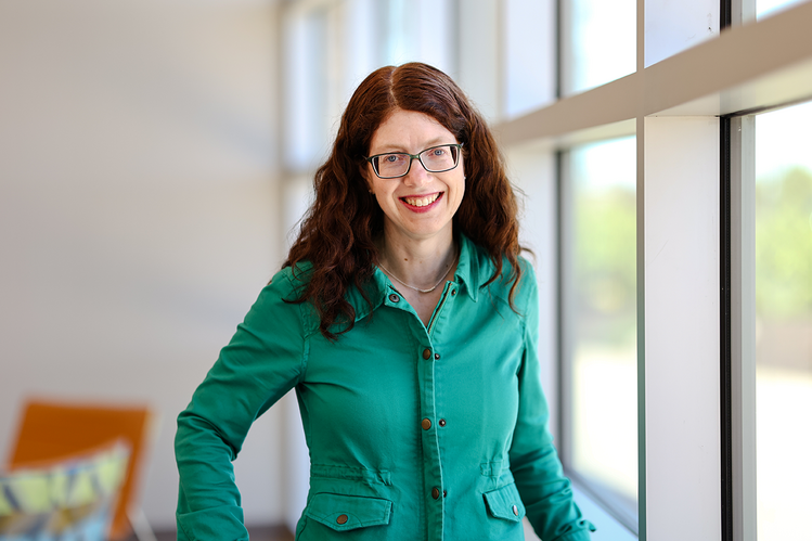 Headshot of Amy standing in front of a window in a green shirt. 