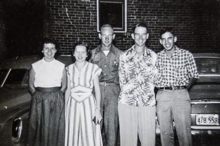 Five young people stand beside a car in a black and white photo. 
