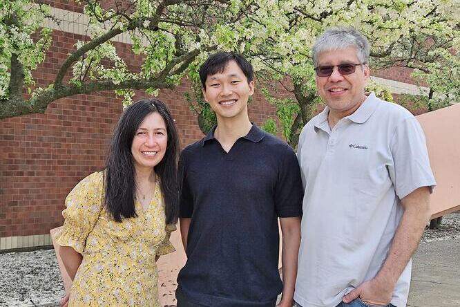 Three individuals standing outside in front of a wall and a tree