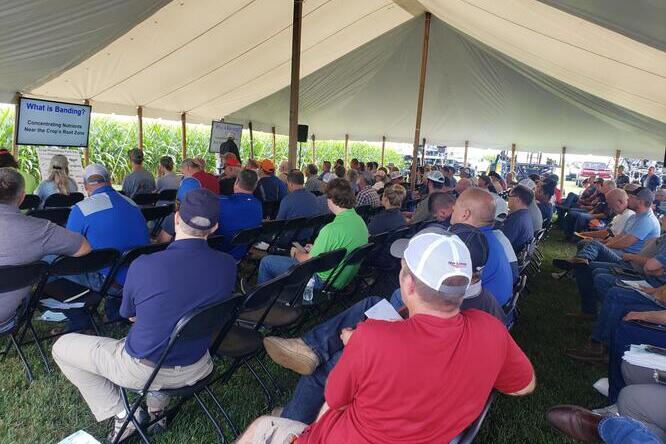 A group of people sit together inside a tent facing the front and listening to speaker.