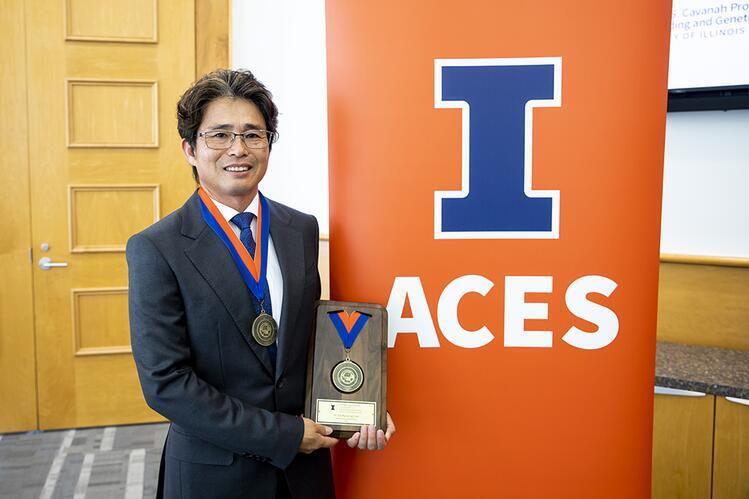 D.K. Lee holds his medallion beside an ACES banner.