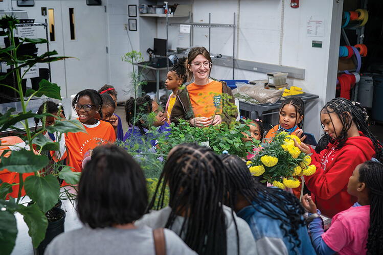 A group of kids gather around a table of plants.