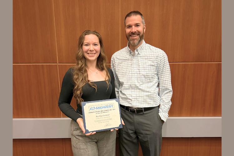 Kaitlyn Sommer (left) and Ryan Dilger (right) A man and woman standing in front of a brown background. The woman is holding a certificate