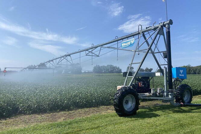 A large irrigation machine waters crops in a green field under a clear blue sky.