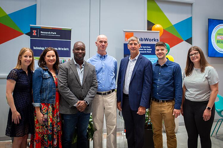 Seven individuals stand together in front of pull up banners and brightly colored graphics. 