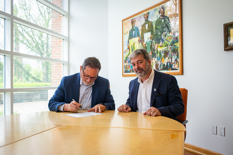 College of ACES Dean Germán Bollero (left) and IFAJ Vice President Adalberto Rossi sign an agreement to develop a Global Certificate in Agricultural Communications, marking a historic step toward launching the James F. Evans Global Center for Food and Agricultural Communications at Illinois. Two men sit at a table signing a document.